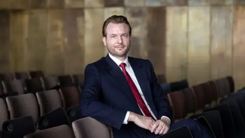 Billede af partner Thomas Melchior Fischer, der sidder ned i mørkeblåt jakkesæt med rødt slips