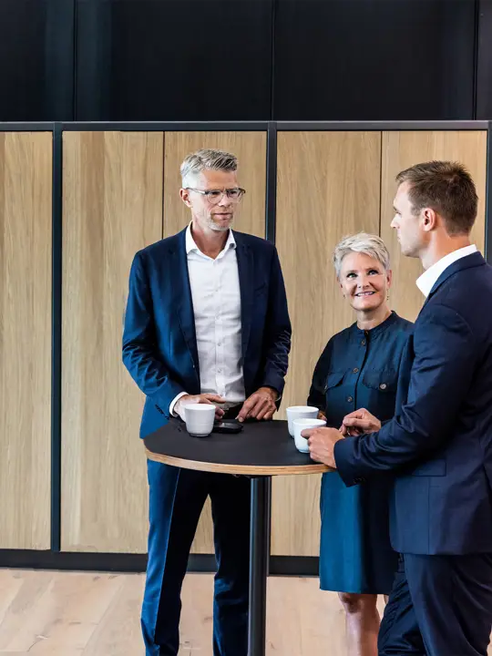 Tre medarbejdere fra Poul Schmith/Kammeradvokaten står omkring et bord og snakker sammen.