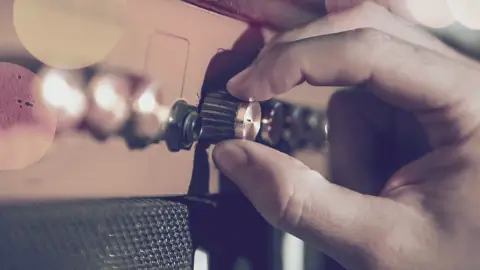 Billede i rødlige nuancer af en hånd skruer op for lyden på en musikafspiller