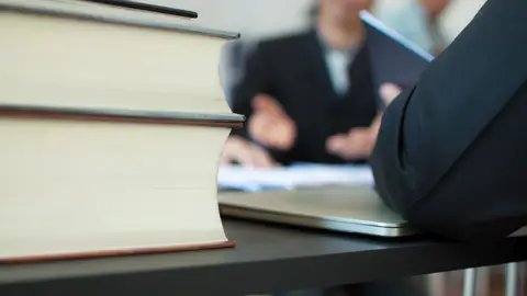 Bøger på et bord mens to personer holder møde