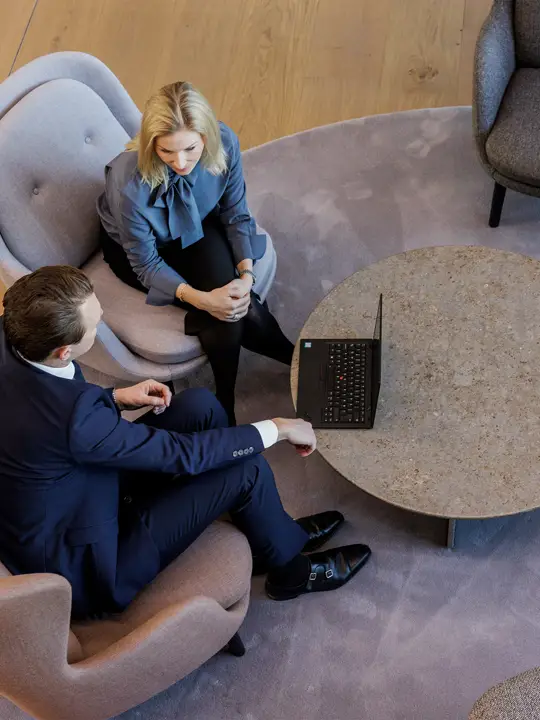 Two employees from Poul Schmith are seen from above as they sit in armchairs and talk to each other.