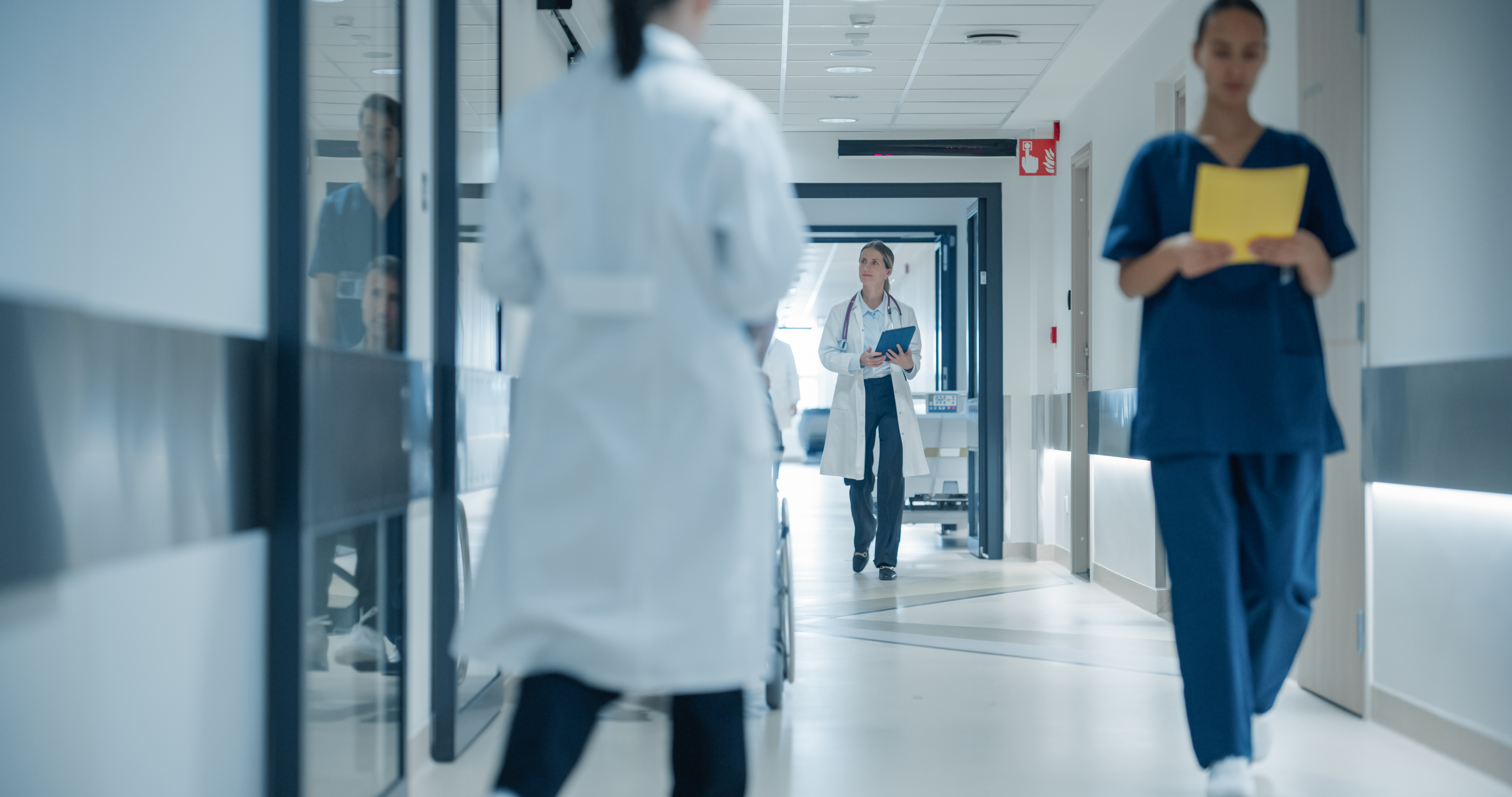 Sundhedspersonale går gennem en hospitalsgang med læger og sygeplejersker i arbejde på et moderne hospital.