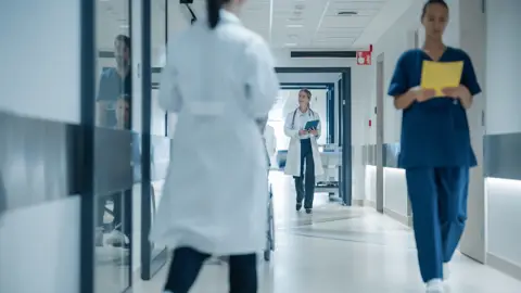 Sundhedspersonale går gennem en hospitalsgang med læger og sygeplejersker i arbejde på et moderne hospital.
