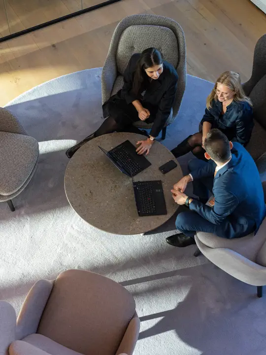 Tre medarbejdere fra Poul Schmith/Kammeradvokaten ses fra oven, mens de sidder i lænestole og snakker sammen.