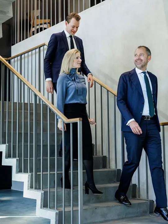 Tre medarbejdere fra Poul Schmith/Kammeradvokaten går ned af en trappe og snakker sammen.