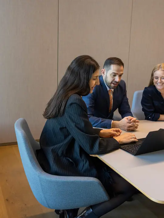 Three lawyers from Poul Schmith are sitting in a meeting room looking at two computers.